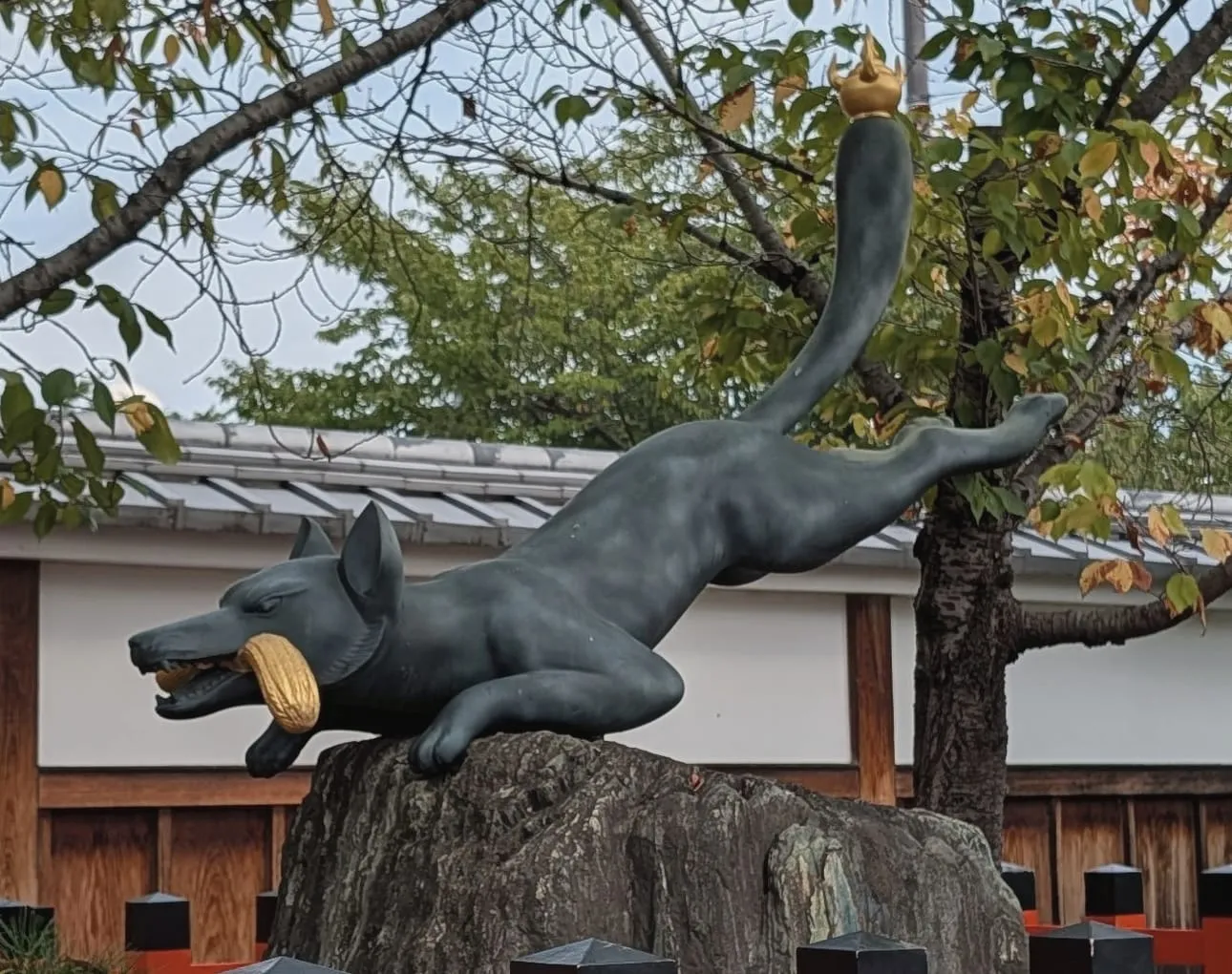 A leaping bronze fox with golden ears of rice in its mouth and a golden jewel on the tip of its tail, at Fushimi Inari, August 22, 2026
