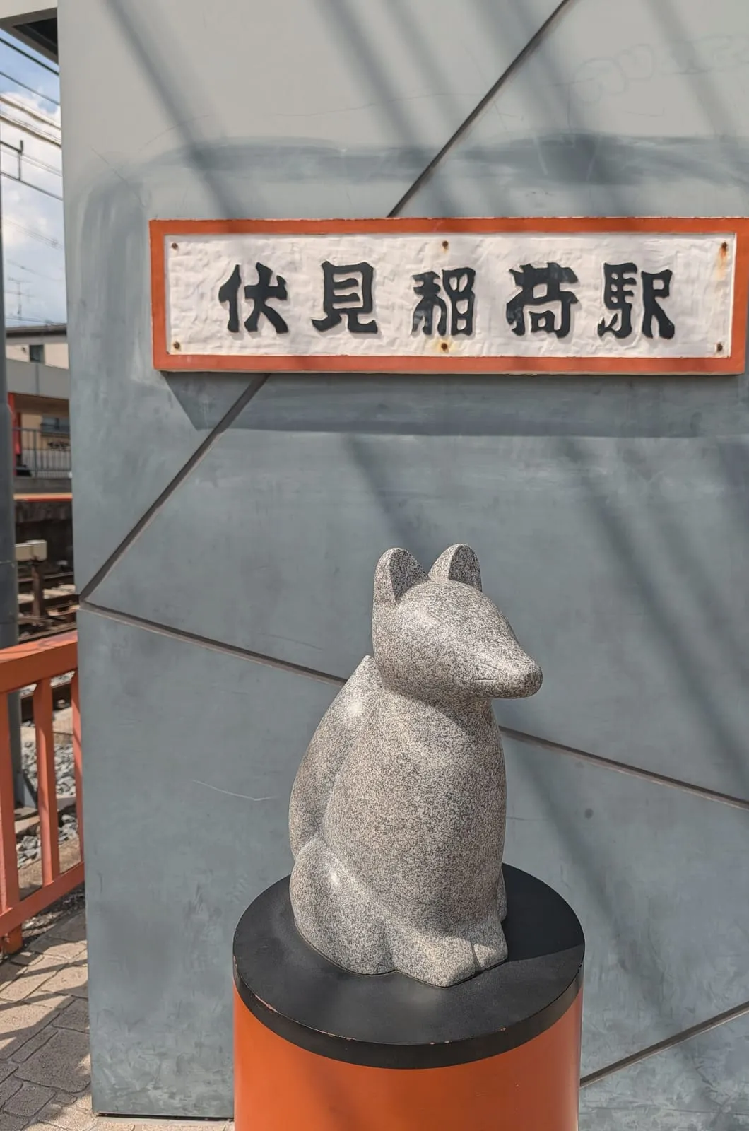 The station sign for Fushimi-Inari and a stone fox statue on the Keihan line, August 22, 2026