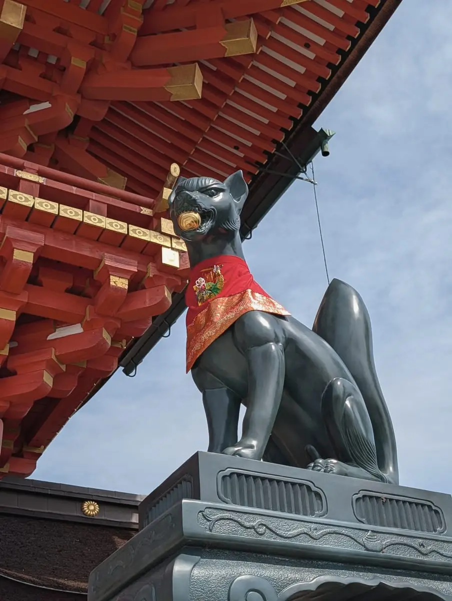 A bronze fox statue below the eaves of a shrine building