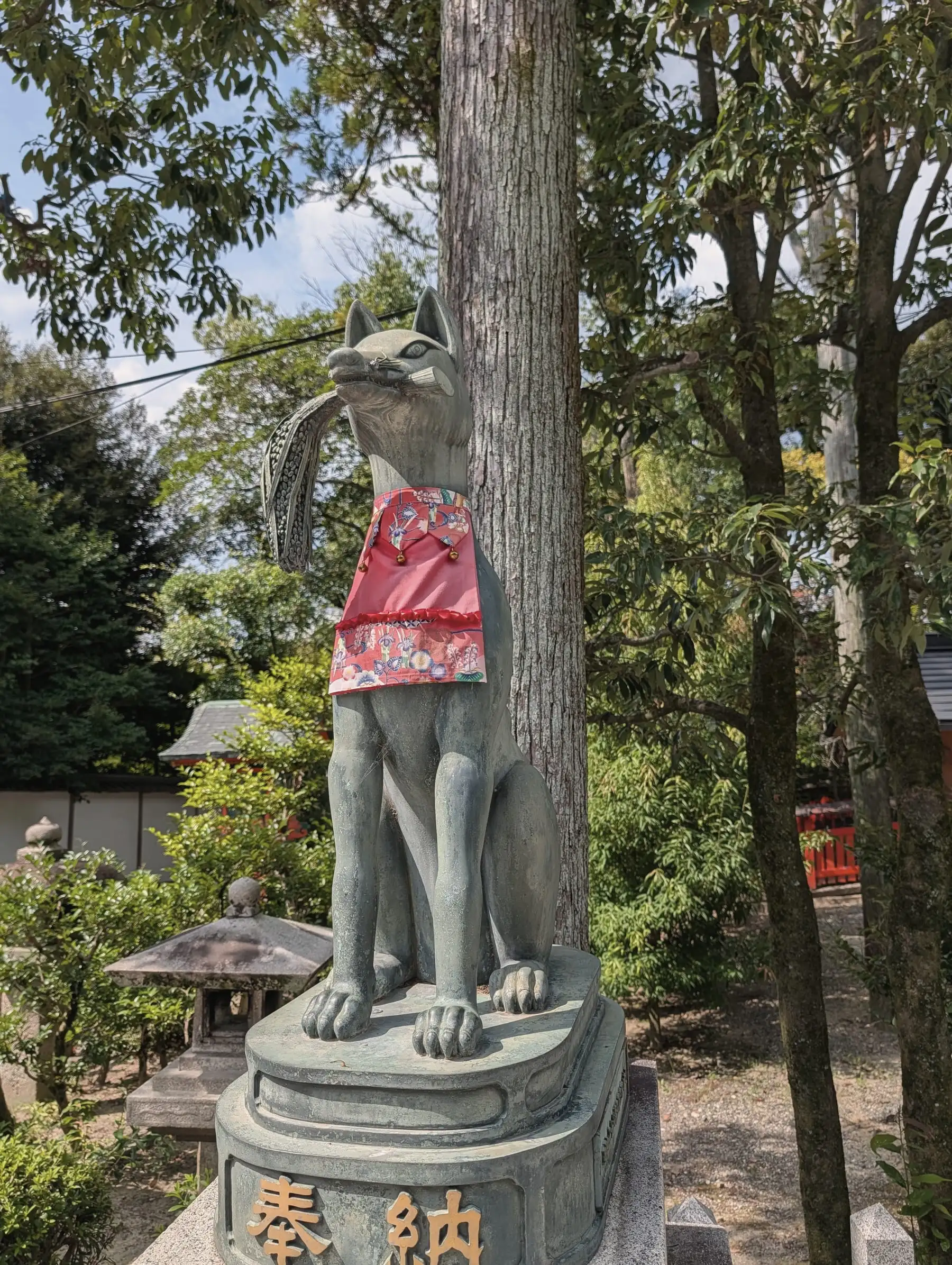 A bronze fox statue standing among trees on the shrine grounds