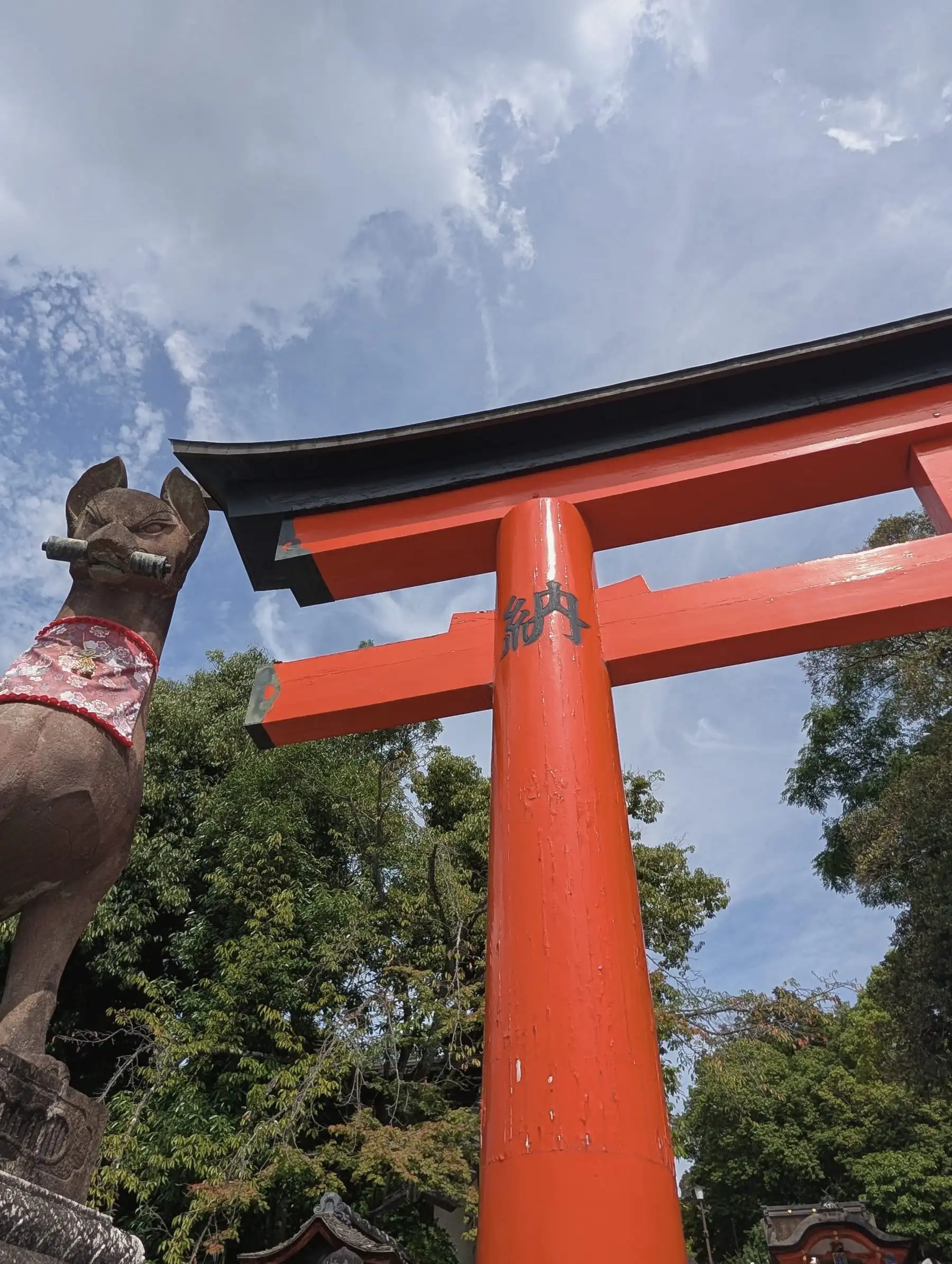 A fox statue and a large vermilion torii gate against the sky