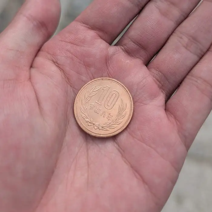A ten-yen coin held in an open palm before making an offering
