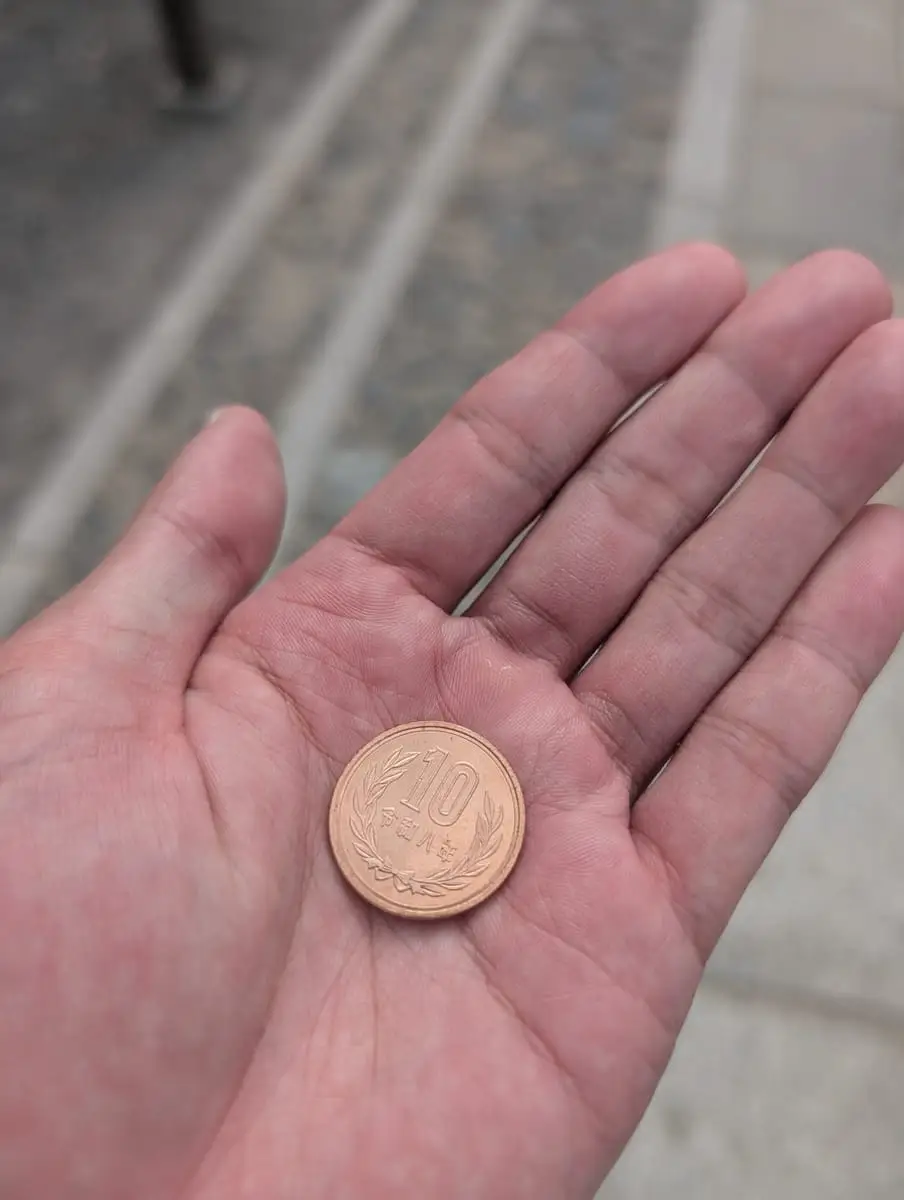 A ten-yen coin held in an open palm before making an offering
