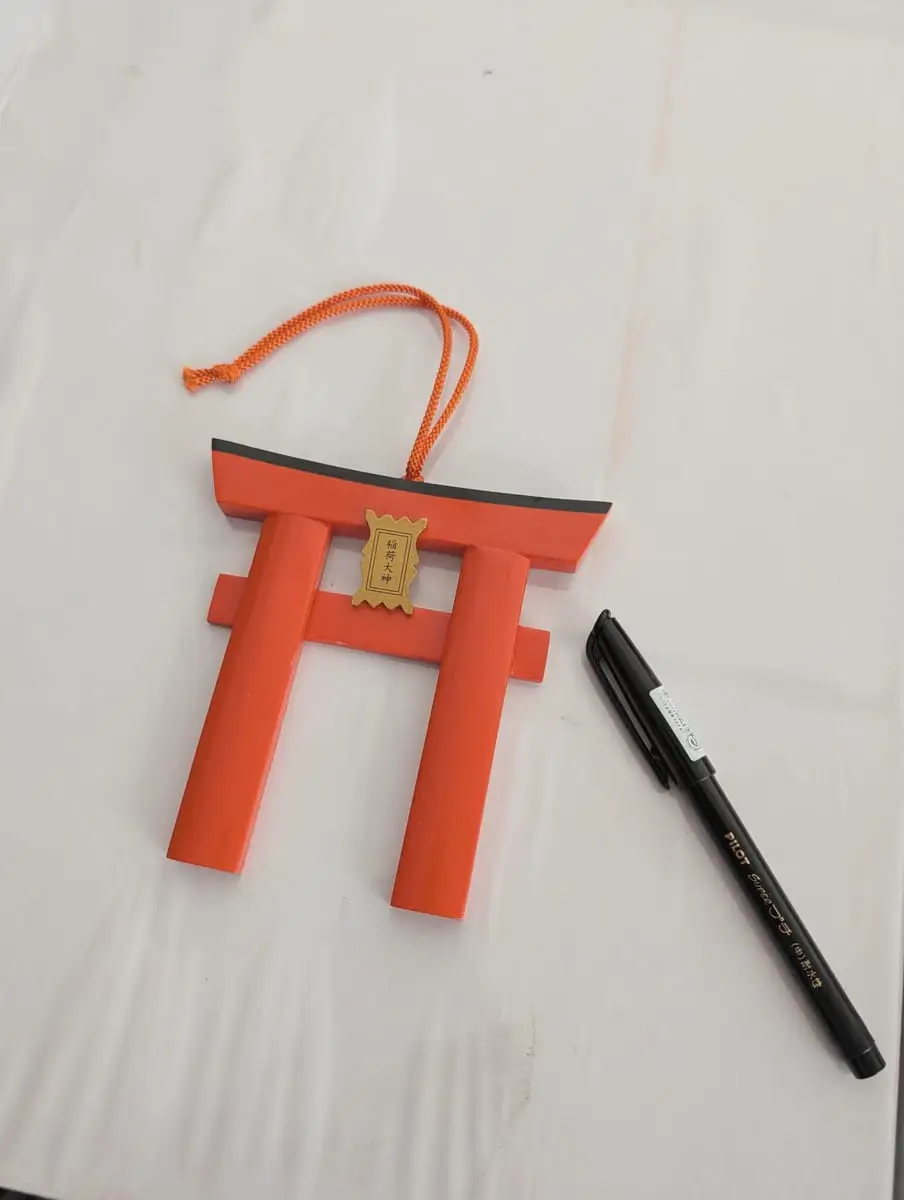A torii-shaped wooden votive tablet and a pen